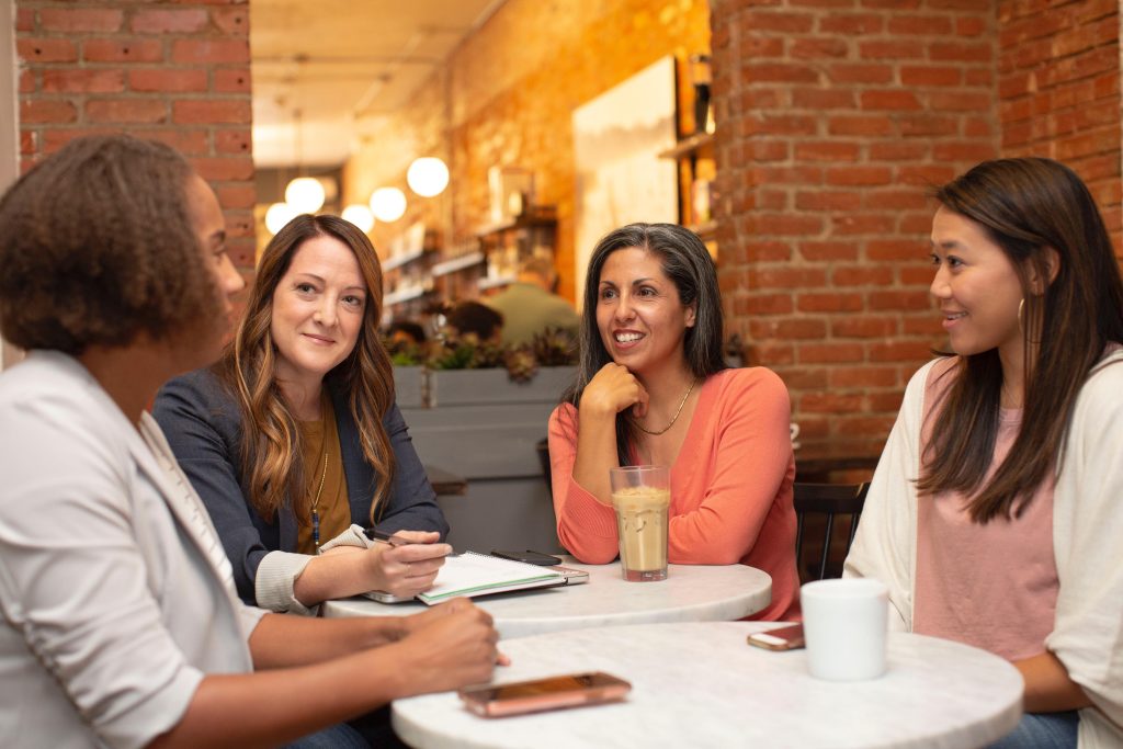 4 women sitting round a table in a group meeting, smiling and looking engaged in the discussion